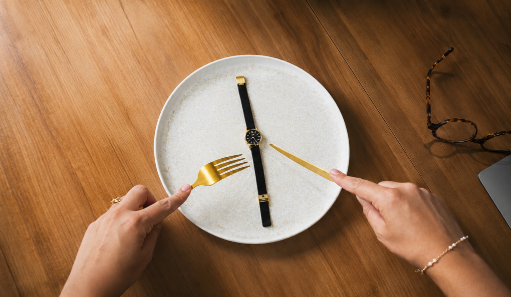 Personne tenant une fourchette et un couteau au-dessus d'une assiette vide contenant une montre, symbole du manque de temps et des difficultés à manger équilibré dans un quotidien chargé.